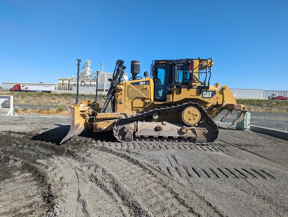 A Cat D6T XL dozer with grade-control mast, parked on a graded pad against a clear blue Southern Idaho sky